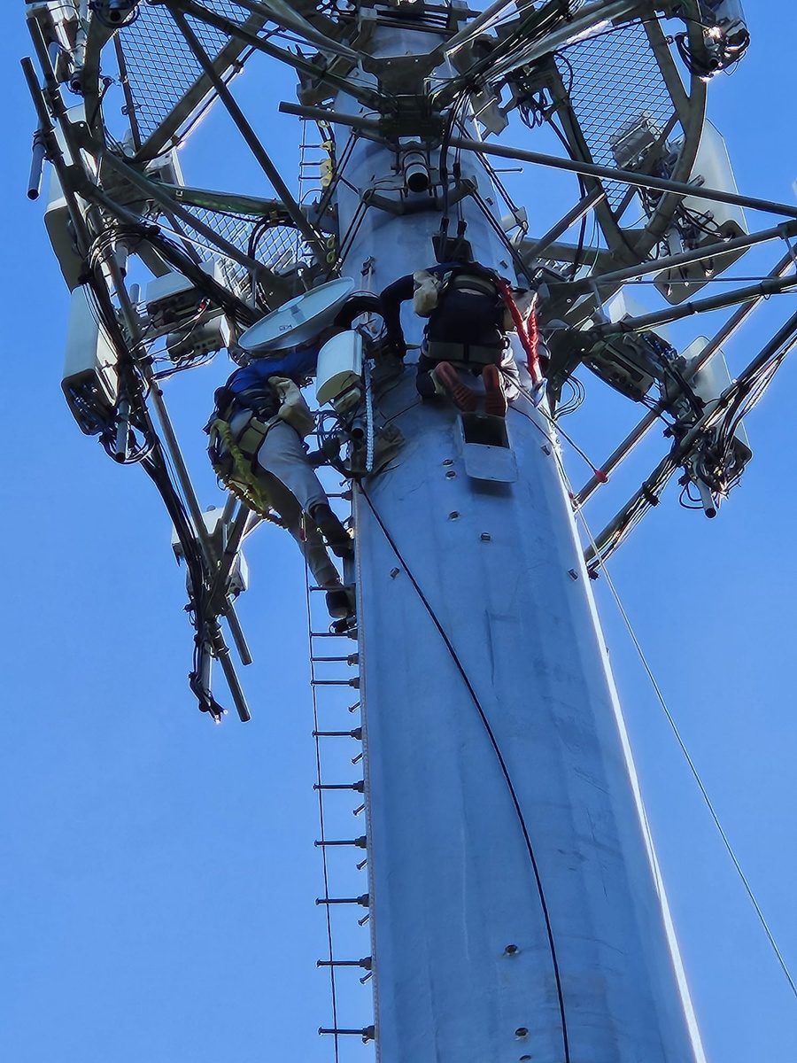 Técnicos de DMwireless trabajando en una torre de telecomunicaciones bajo cielo azul